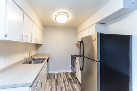A black refrigerator sits in a kitchen with white cabinets and a sink.