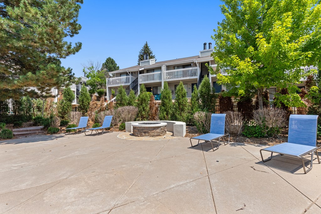a patio with blue chairs and a fire pit and a building in the background