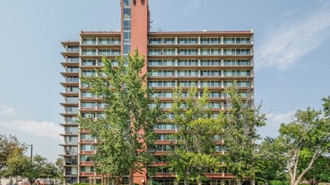 A tall red building with many windows and trees in front.