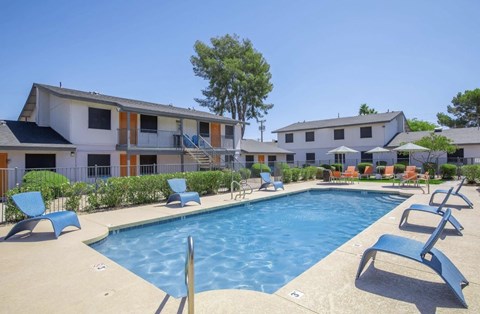 A swimming pool surrounded by lounge chairs and buildings.
