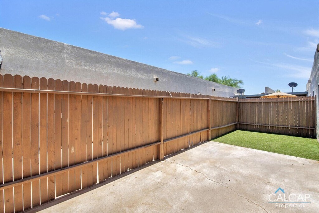 A backyard with a wooden fence and a concrete ground.
