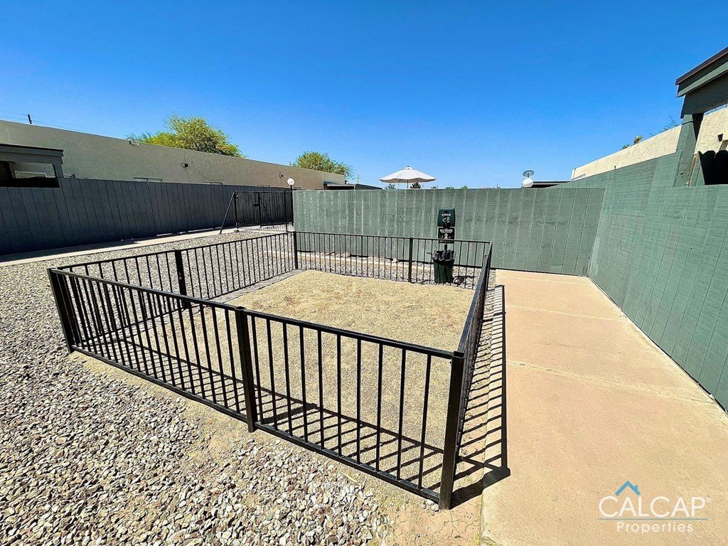 A black metal fence encloses a gravel area in a sunny outdoor setting.