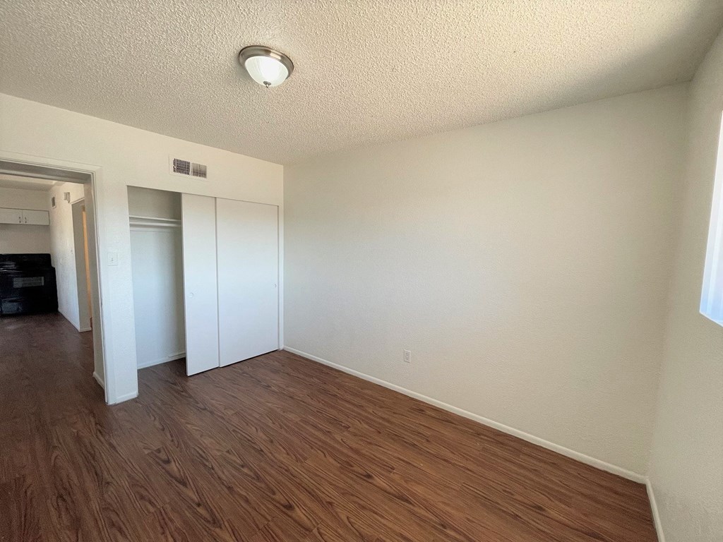 A room with white walls and wood flooring, with a doorway leading to another room.