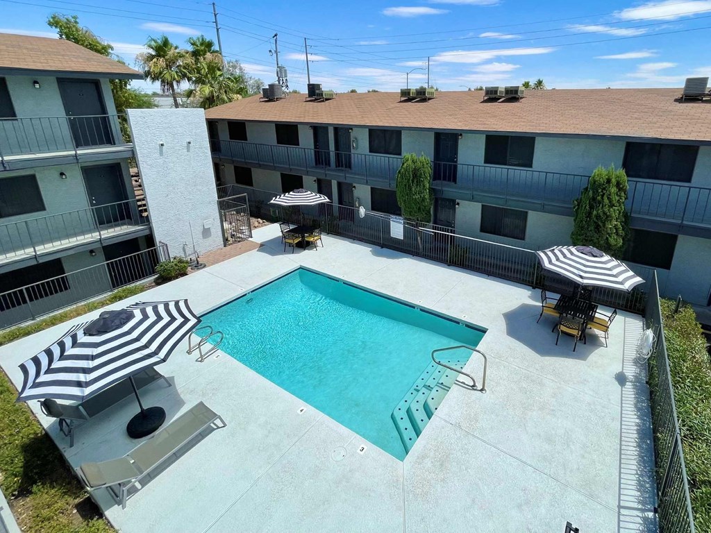 A swimming pool surrounded by a patio with chairs and umbrellas.