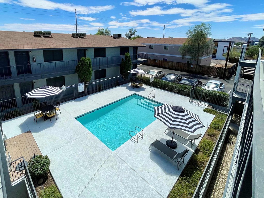 A pool surrounded by chairs and umbrellas in a sunny courtyard.
