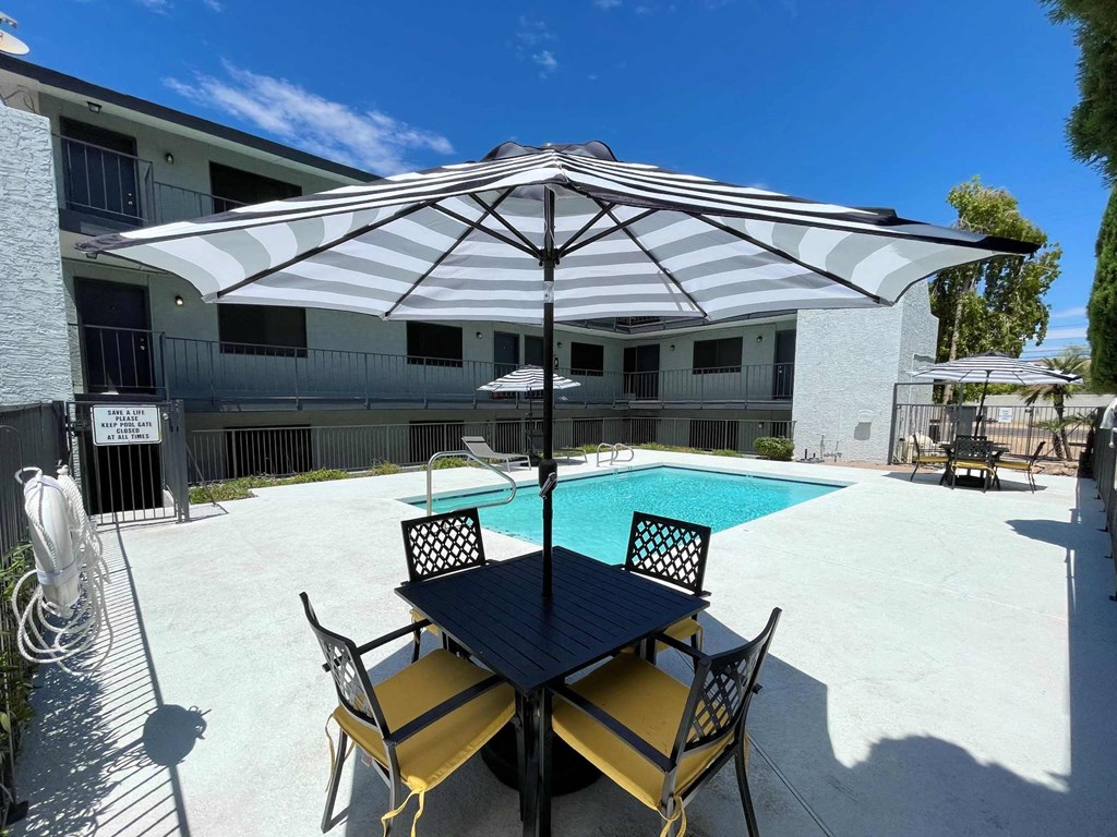 A poolside table with chairs and an umbrella is set up by a pool.