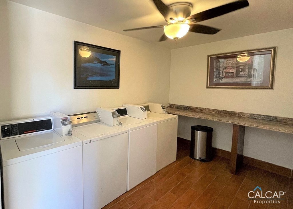 A laundry room with a washer and dryer, a trash can, and a ceiling fan.