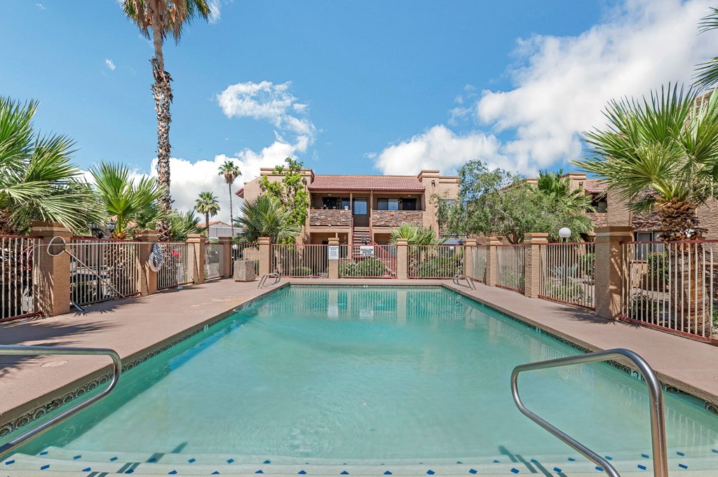 A pool surrounded by palm trees and a building in the background.