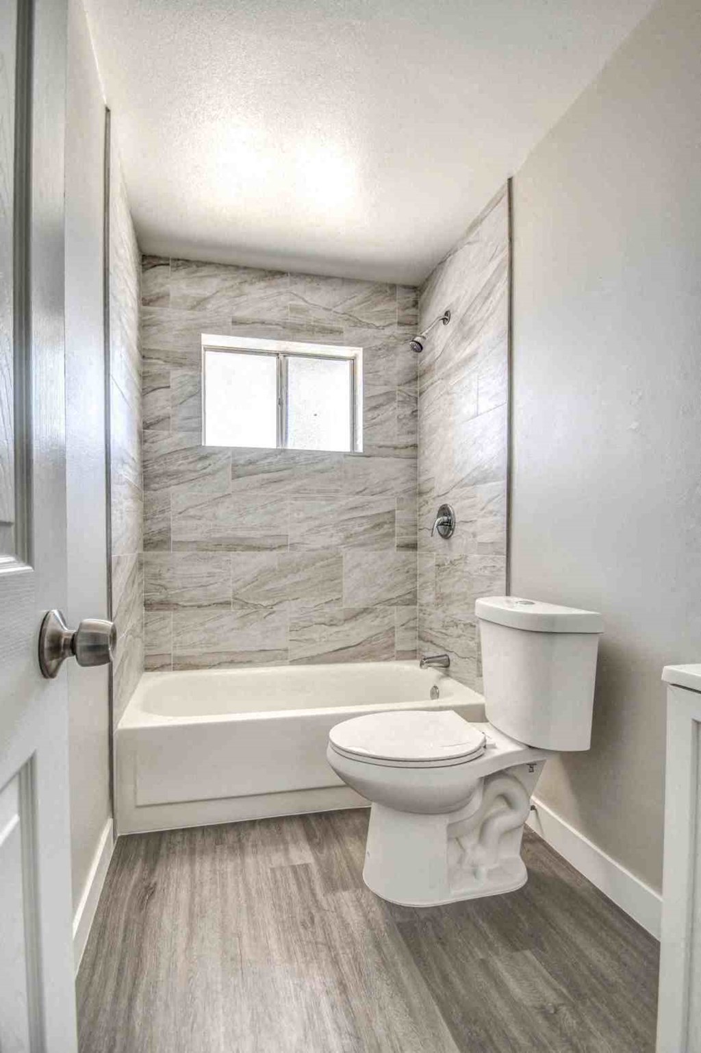 A white toilet in a bathroom with a marble wall and a window.