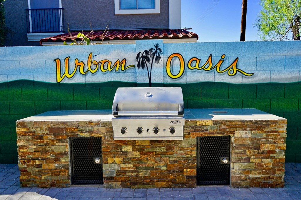 A wall with a mural of a beach and the words "Urban Oasis" above a built in BBQ grill.