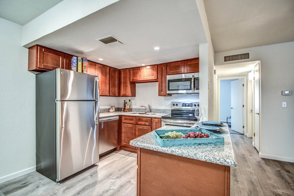 A kitchen with a refrigerator, microwave, and wooden cabinets.