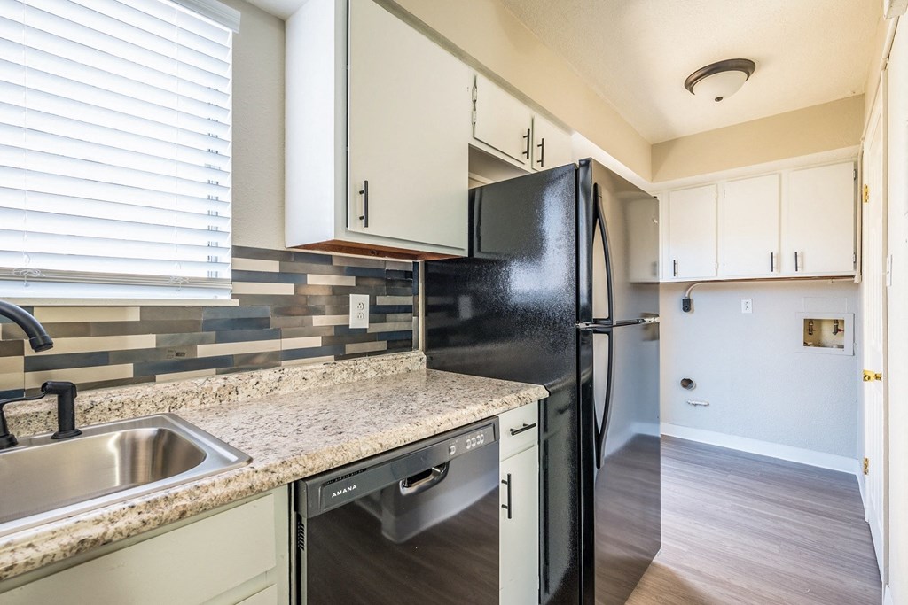 A black fridge in a kitchen with a sink and a dishwasher.