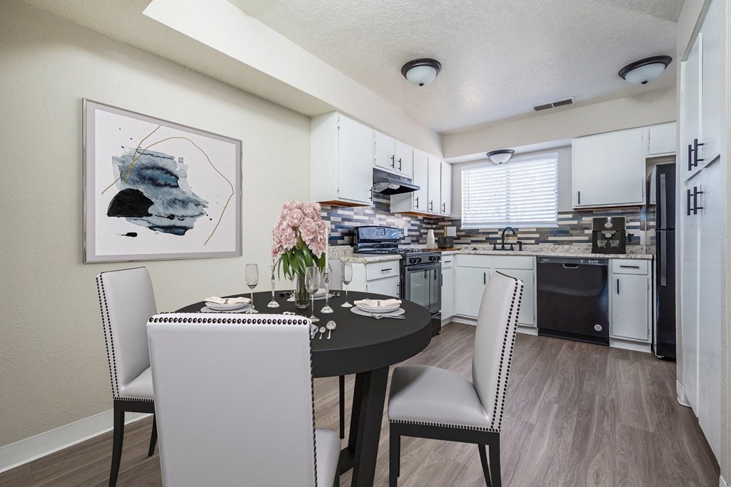 A dining room with a table set for two and a kitchen in the background.
