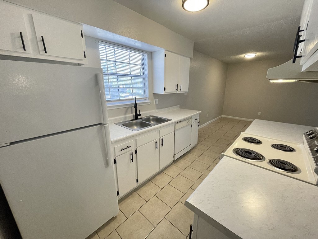 A white kitchen with a refrigerator, sink, and stove.