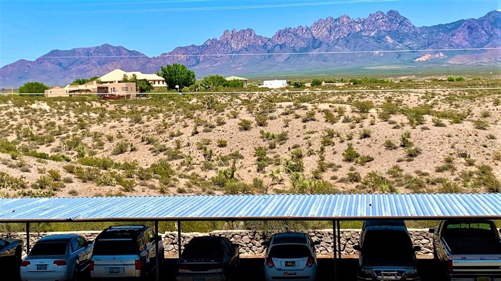 A parking lot with cars and a house in the desert with mountains in the background.