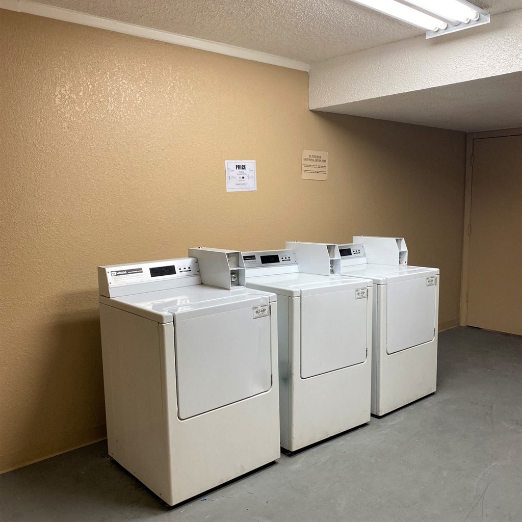 Three washing machines are lined up in a laundry room.