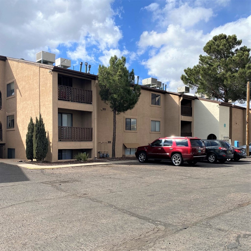 A red car is parked in front of a building with a balcony.