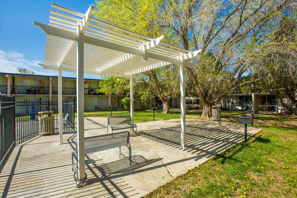 A white pergola is in the middle of a grassy area.