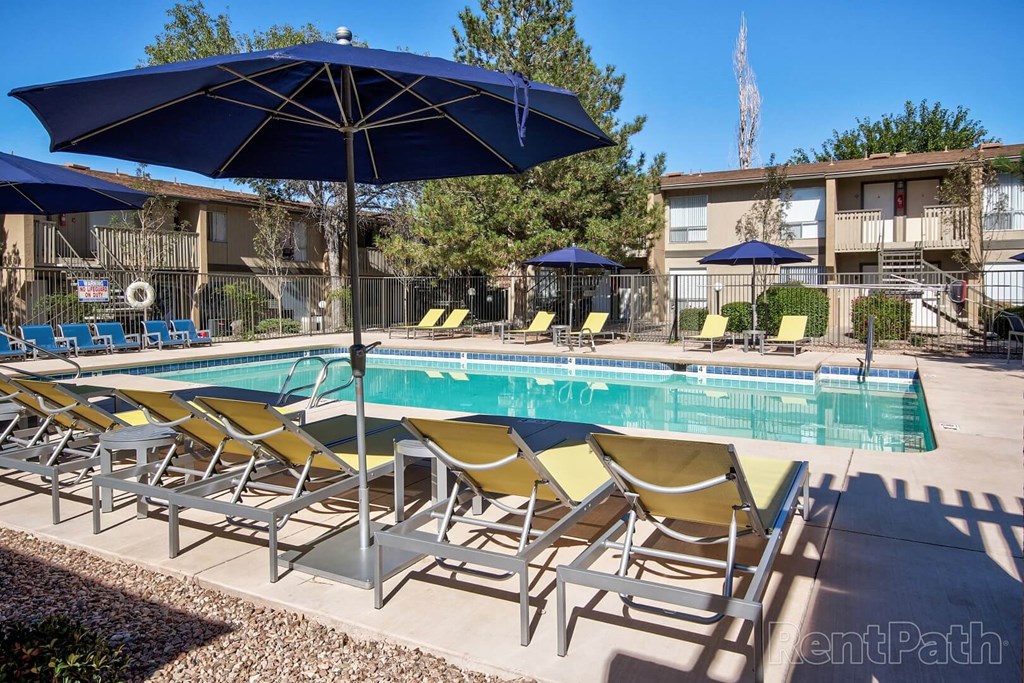 A pool with yellow chairs and blue umbrellas.