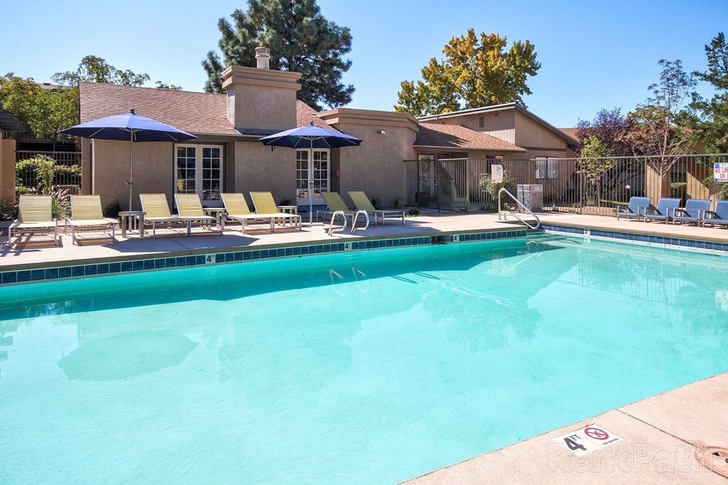 A pool with a blue umbrella and chairs.