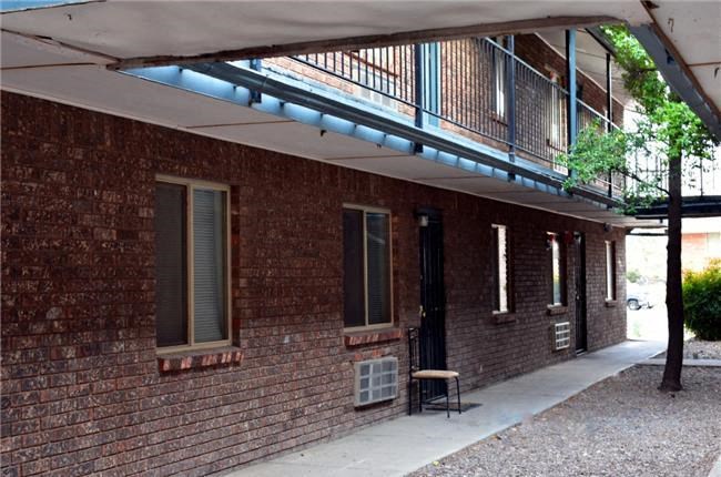 A brick building with a balcony and a tree in front.