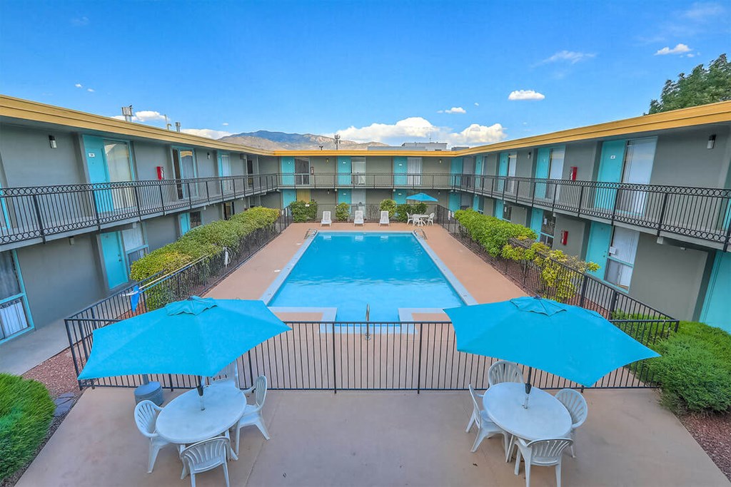 A pool surrounded by a fence and chairs with umbrellas.