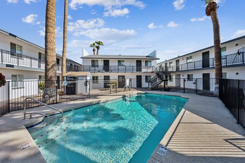 A swimming pool surrounded by palm trees and apartment buildings.