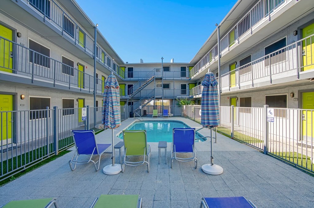A pool surrounded by chairs and umbrellas in a courtyard.