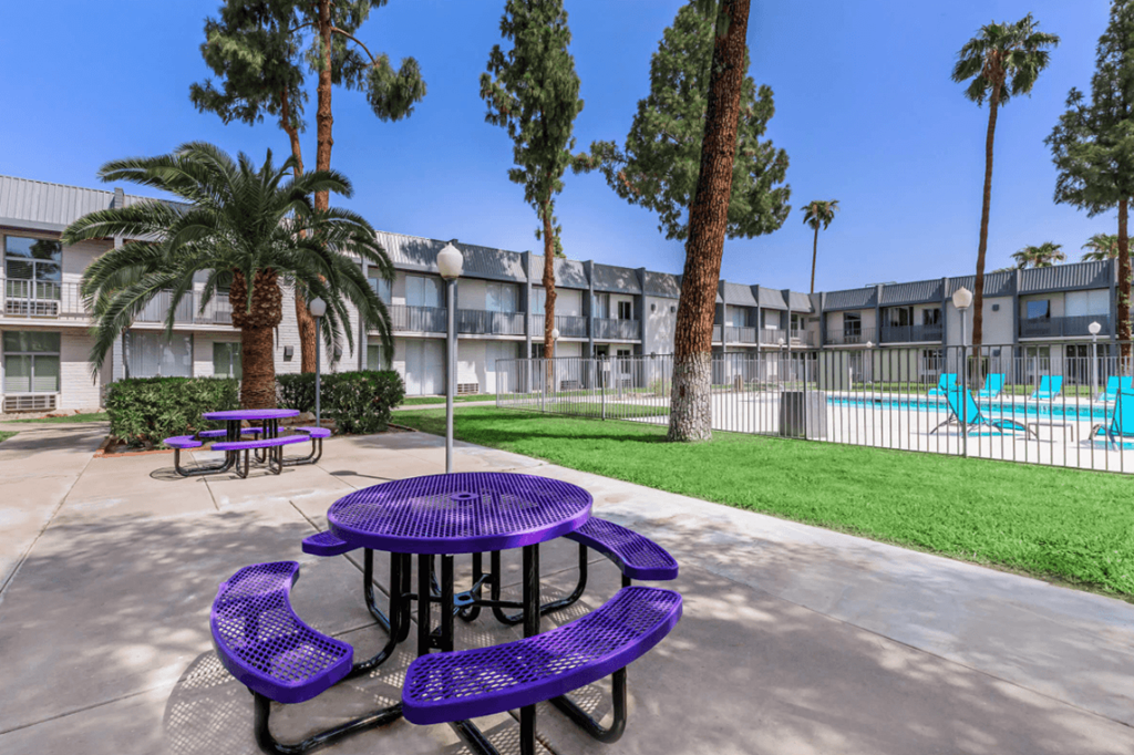 Purple picnic tables are surrounded by palm trees and a pool.