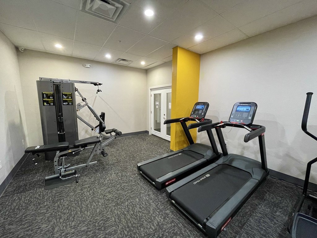 A gym with treadmills, a weight machine, and a yellow wall.