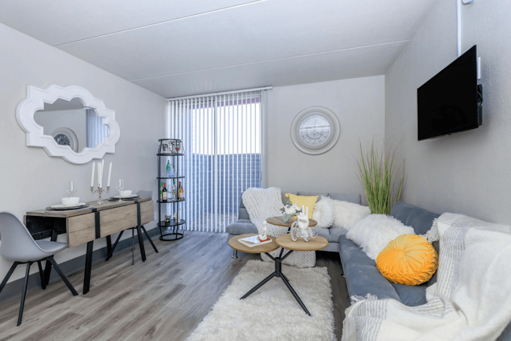 A modern living room with a grey sofa, a wooden coffee table, and a TV mounted on the wall.