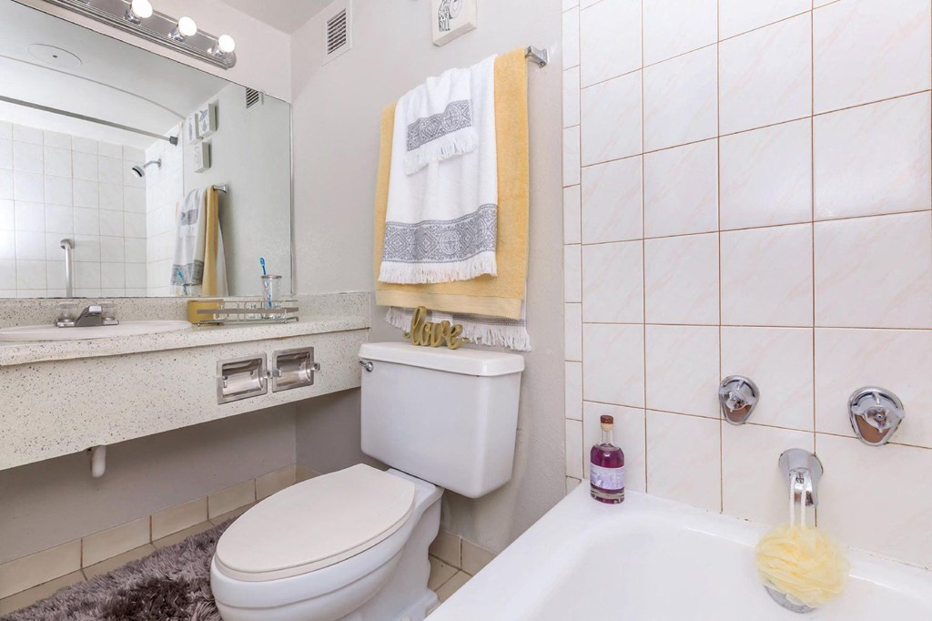 A white toilet sits in a bathroom with a white sink and a white towel hanging on the wall.