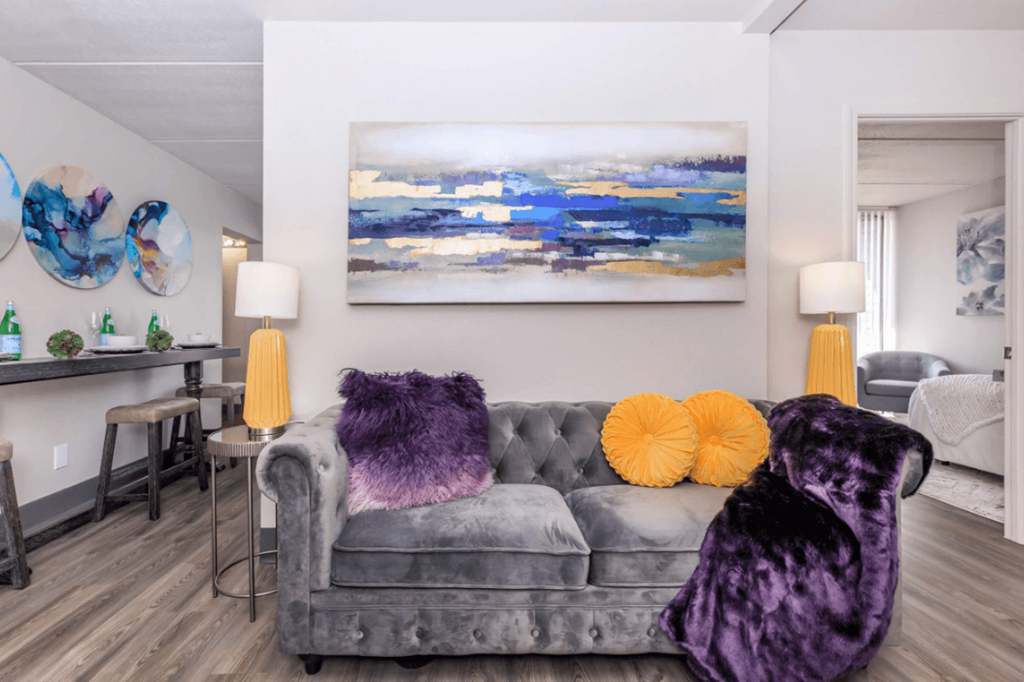 A grey couch with purple and orange pillows in a living room.