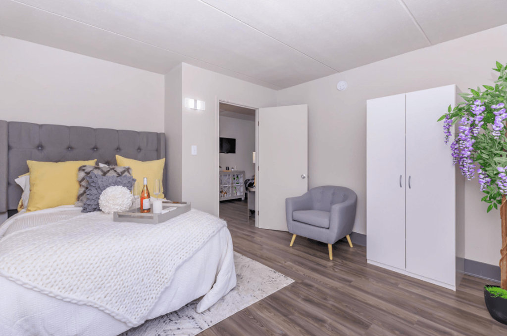 A bedroom with a bed, chair, and a plant.