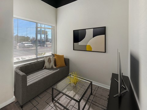 A living room with a grey couch, a glass coffee table, and a painting on the wall.