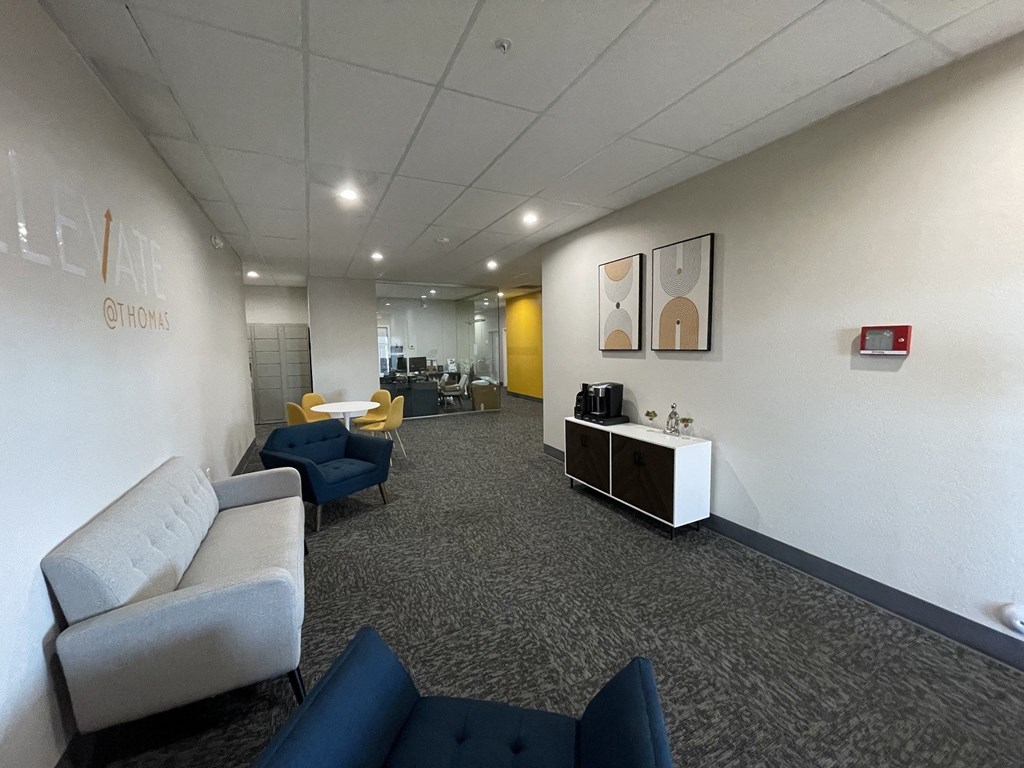 A conference room with a carpeted floor and a white wall with a sign that says "Elevate @ Thomas".