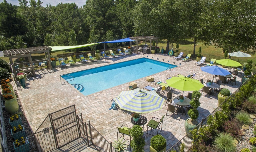 A large outdoor swimming pool surrounded by a patio area with chairs and umbrellas.