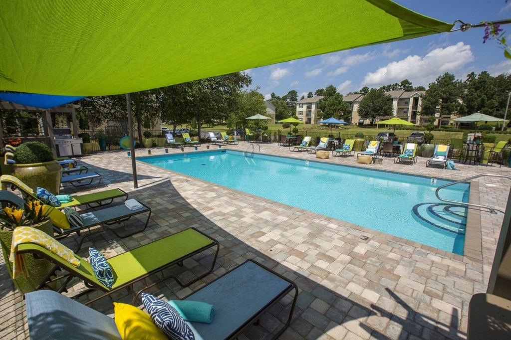 A pool area with a green umbrella and lounge chairs.
