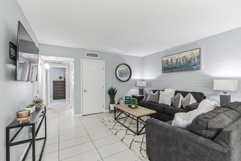 A living room with a grey couch and a painting on the wall.
