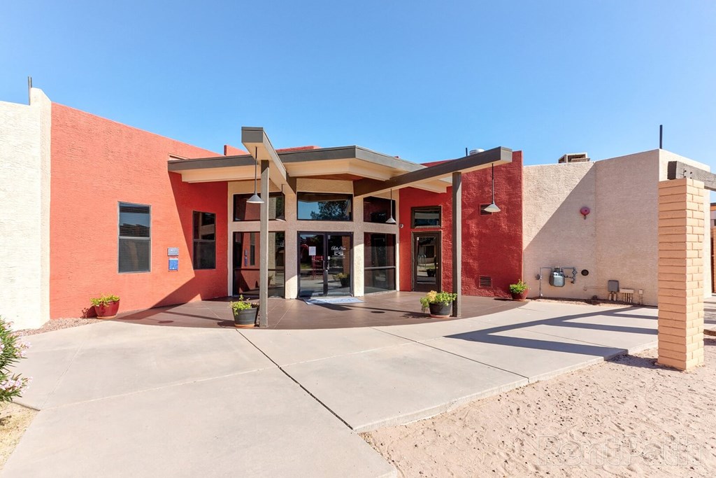 A building with a red and beige exterior has a covered walkway leading to the entrance.