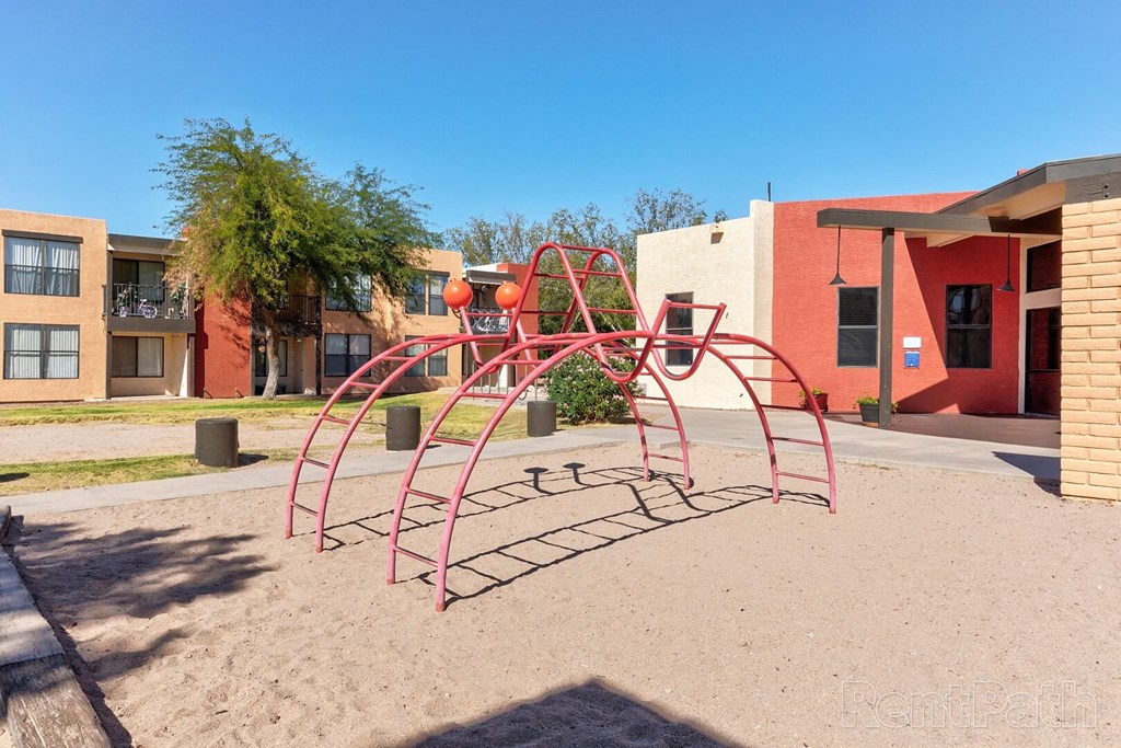 A playground with a red swing set in front of a building.