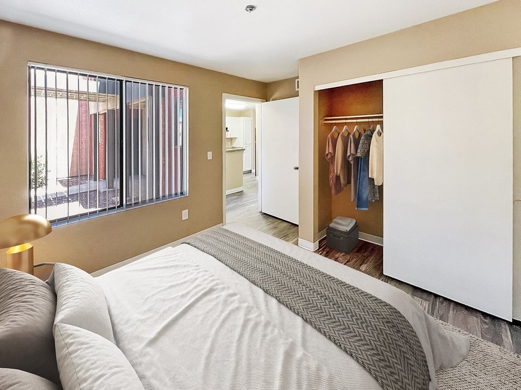 A bedroom with a large bed and a wardrobe with clothes hanging in it.