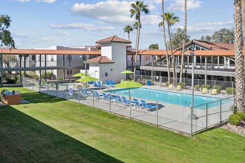 A pool surrounded by a fence with chairs and umbrellas.