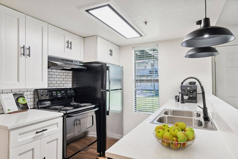 A black stove and refrigerator in a kitchen with white cabinets and a bowl of apples on the counter.