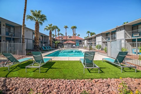 A pool surrounded by palm trees and lawn chairs.