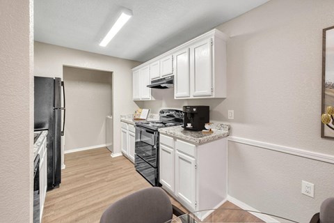 A kitchen with white cabinets and a black fridge.