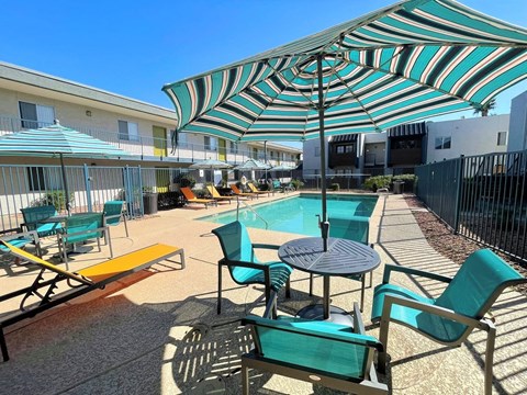 A sunny day at the pool with a striped umbrella providing shade.