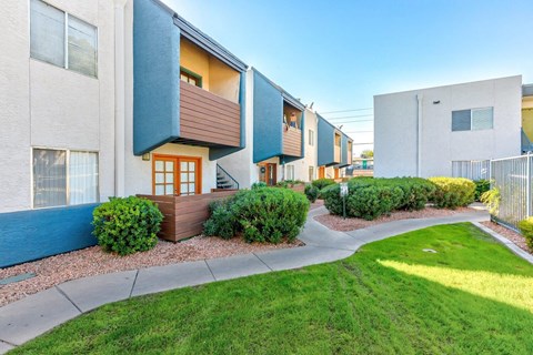 A row of modern townhouses with a sidewalk and green grass in front.