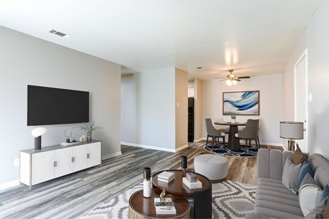 A modern living room with a grey sofa, a wooden coffee table, and a television on a white cabinet.