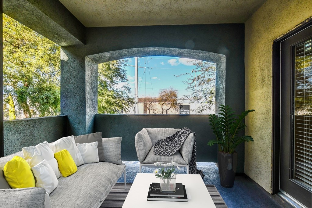 A living room with a grey couch, a white coffee table, and a large window with a view of trees.